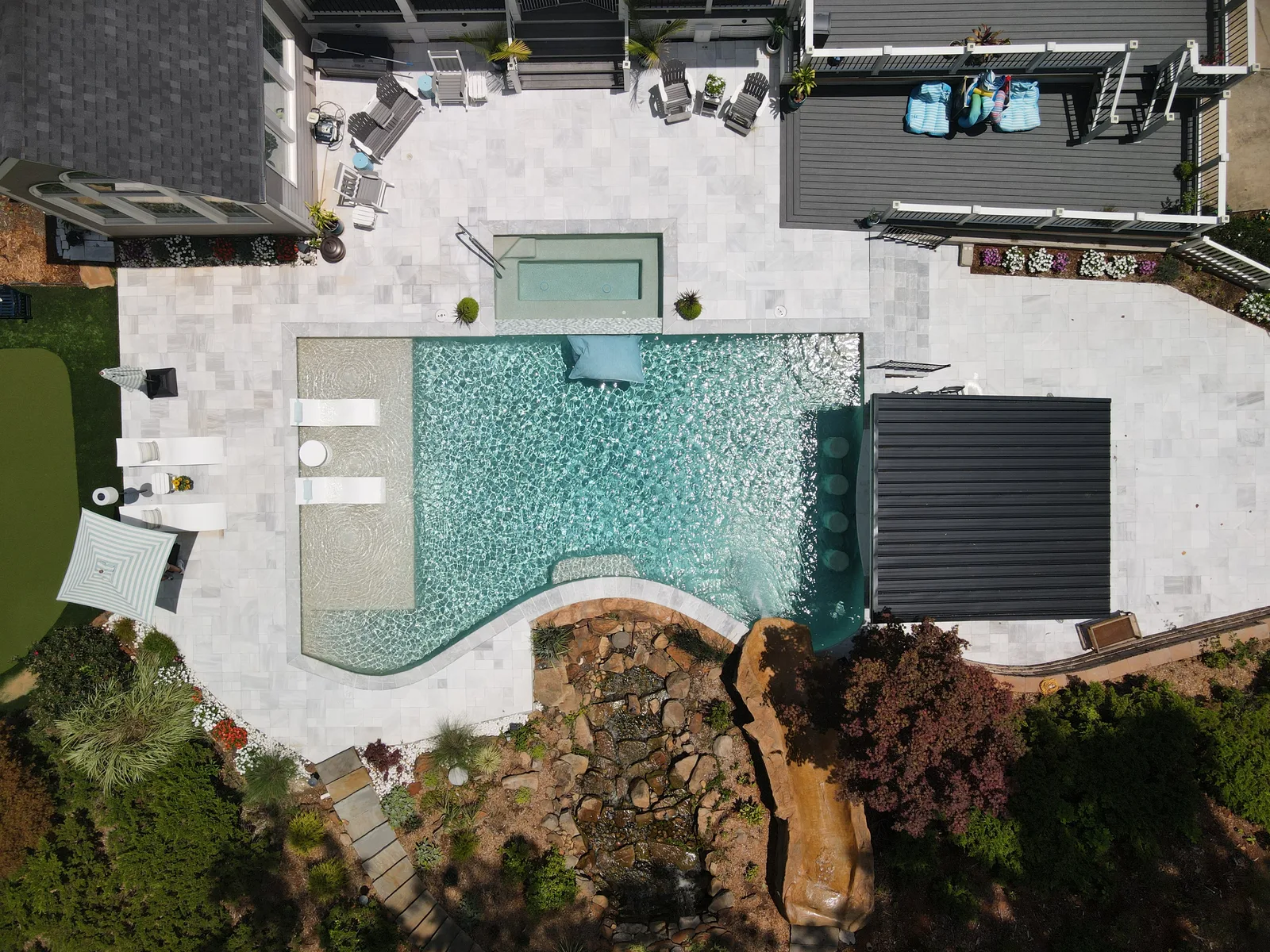 Drone view of a curved RutherfordMade pool with a rock waterfall and green landscaping