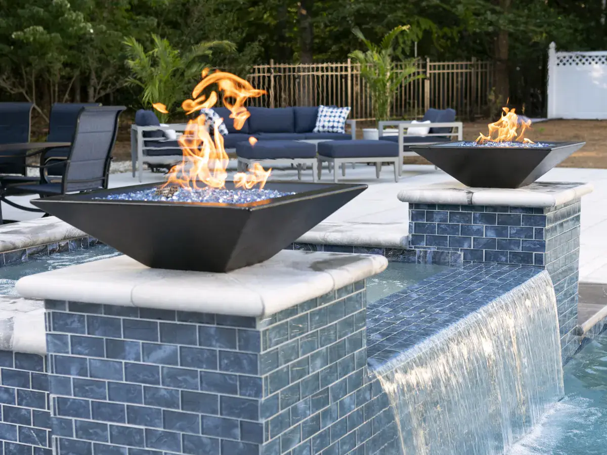Two fire bowls burning on blue-tiled columns above a waterfall spilling into a RutherfordMade pool