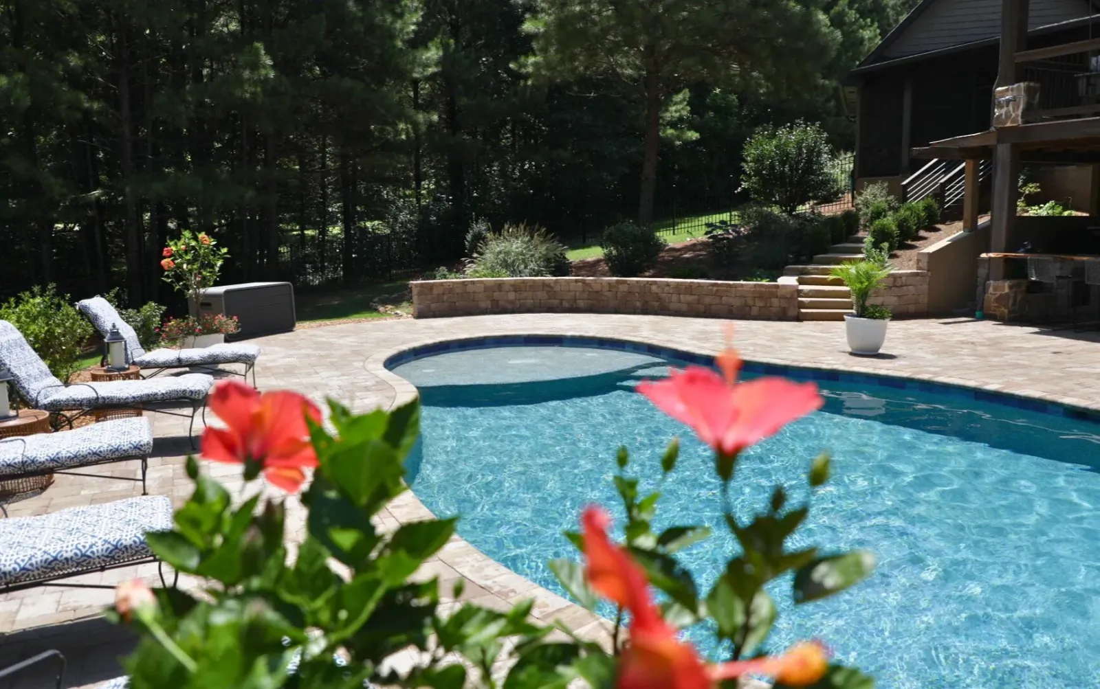 A completed RutherfordMade pool framed by flowers, lounge chairs, and mature trees