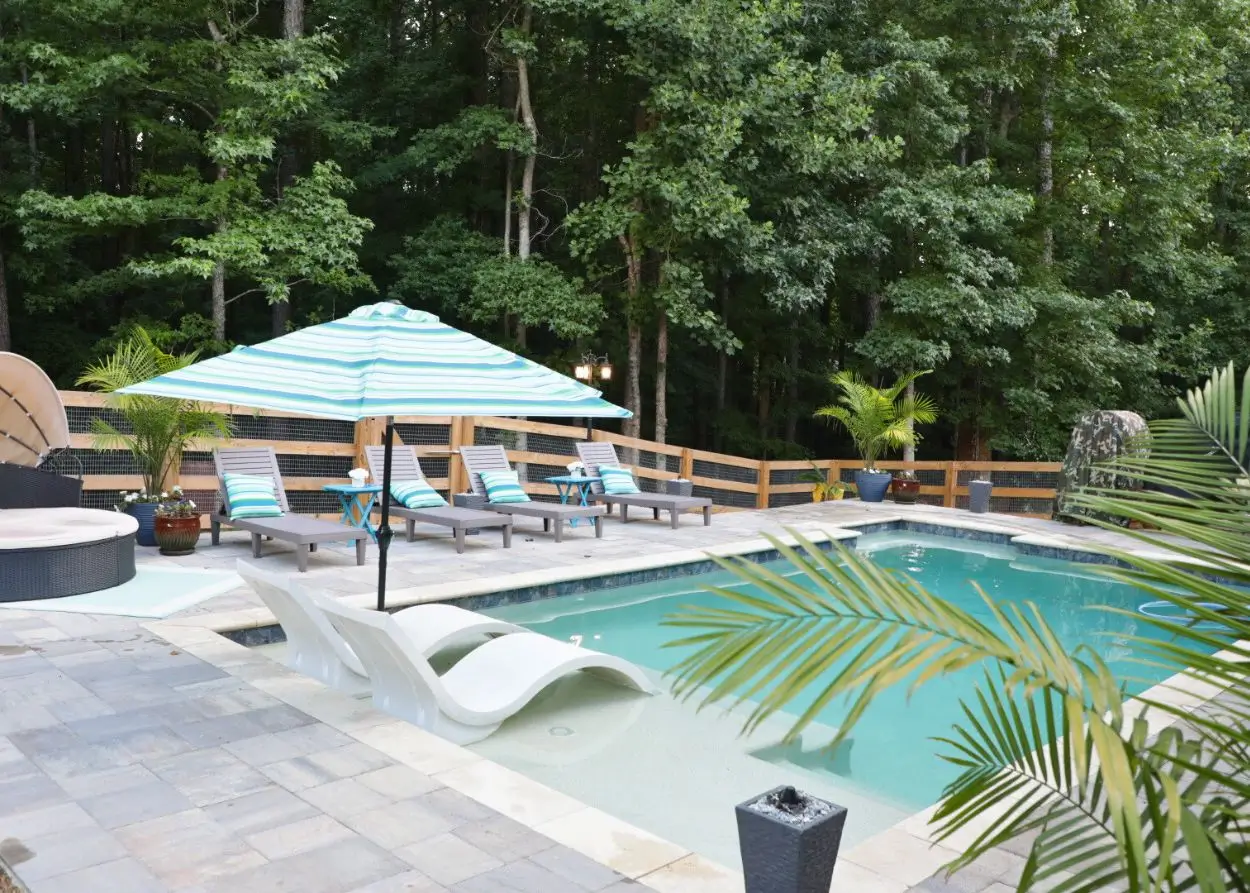 RutherfordMade pool with blue umbrellas, lounge chairs, palm trees, and integrated outdoor living